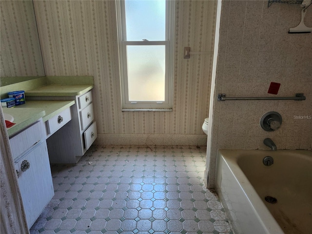 full bath with toilet, a washtub, vanity, baseboards, and wallpapered walls