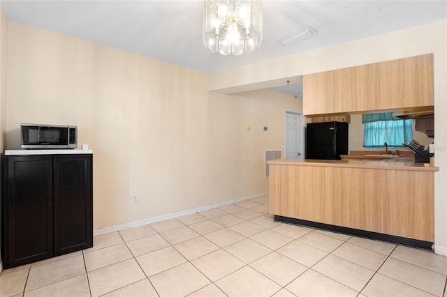 kitchen with black refrigerator, sink, light tile patterned floors, light brown cabinets, and an inviting chandelier