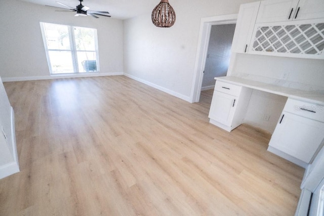 kitchen with white cabinetry, built in desk, ceiling fan, and light wood-type flooring