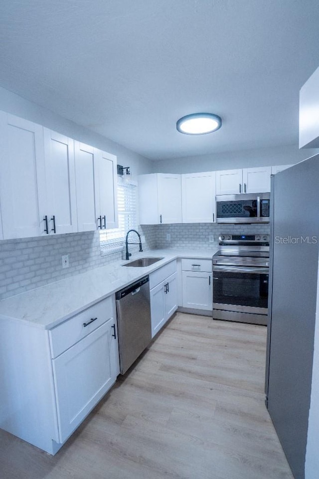 kitchen with sink, white cabinetry, stainless steel appliances, tasteful backsplash, and light hardwood / wood-style floors