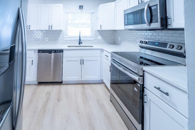 kitchen with sink, light wood-type flooring, appliances with stainless steel finishes, decorative backsplash, and white cabinets