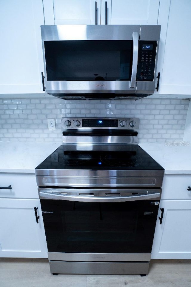 kitchen featuring white cabinetry, light stone counters, decorative backsplash, and stainless steel appliances