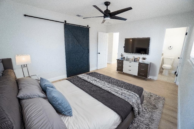 bedroom with ceiling fan, a barn door, a textured ceiling, and ensuite bath