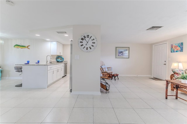 kitchen featuring light tile patterned floors, sink, light stone counters, white cabinets, and a breakfast bar area