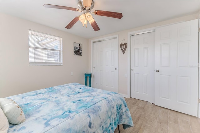 bedroom with ceiling fan, light hardwood / wood-style flooring, and multiple closets