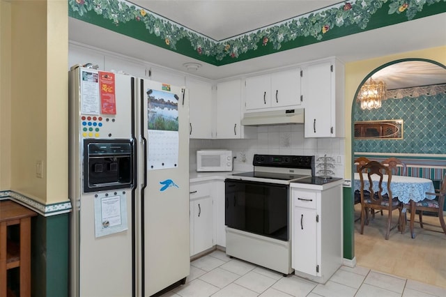 kitchen featuring an inviting chandelier, light tile patterned floors, white cabinets, white appliances, and backsplash