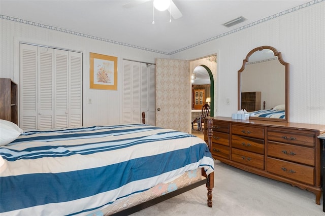 bedroom with two closets, light colored carpet, and ceiling fan