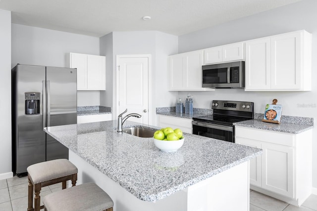 kitchen featuring an island with sink, sink, white cabinets, light stone counters, and stainless steel appliances