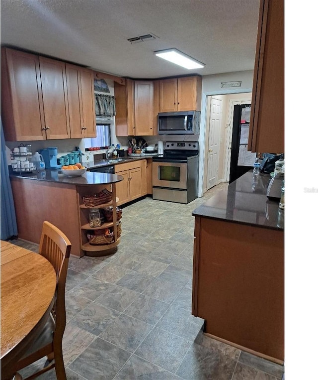 kitchen with appliances with stainless steel finishes, sink, a textured ceiling, and kitchen peninsula