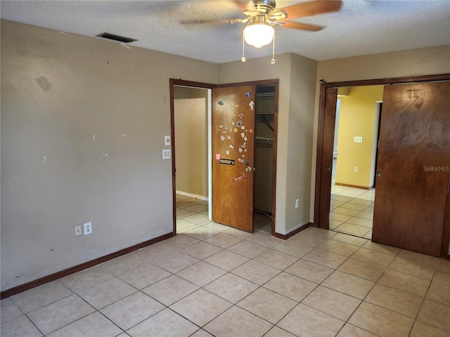 empty room featuring ceiling fan, light tile patterned floors, and a textured ceiling