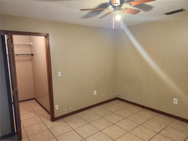 empty room with ceiling fan, light tile patterned floors, and a textured ceiling