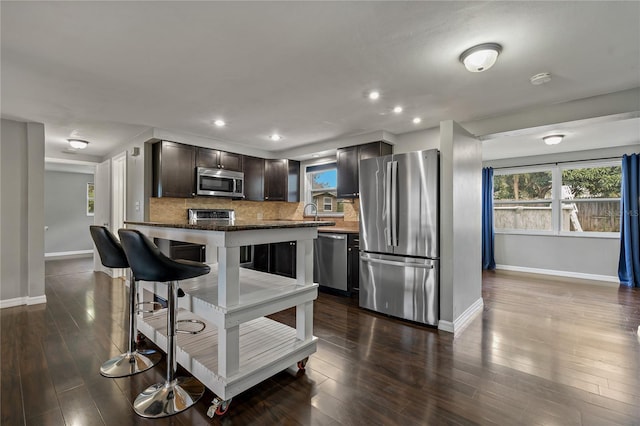 kitchen featuring stainless steel appliances, baseboards, decorative backsplash, dark brown cabinetry, and dark wood-style flooring