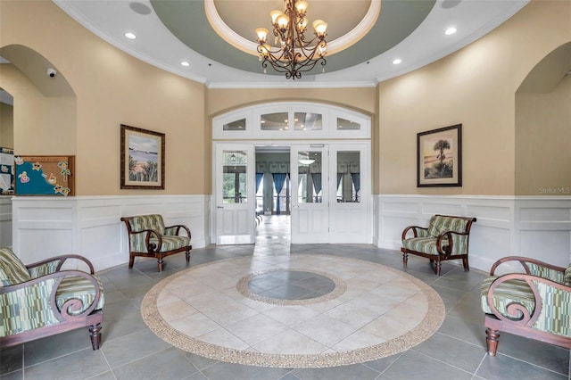 tiled foyer featuring a high ceiling, ornamental molding, an inviting chandelier, and a tray ceiling