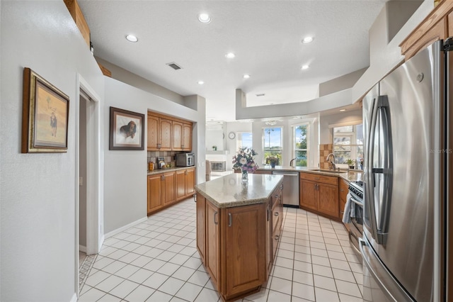 kitchen with sink, appliances with stainless steel finishes, light stone counters, a kitchen island, and light tile patterned flooring