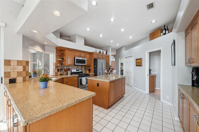 kitchen with sink, light stone counters, a center island, stainless steel appliances, and decorative backsplash