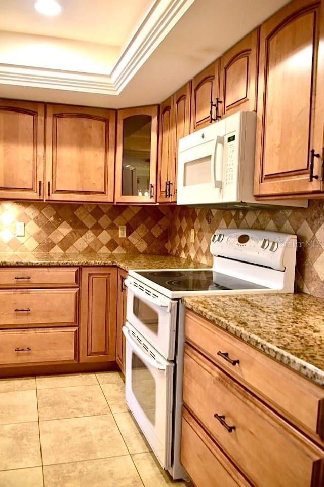 kitchen featuring light tile patterned flooring, light stone counters, a raised ceiling, white appliances, and decorative backsplash