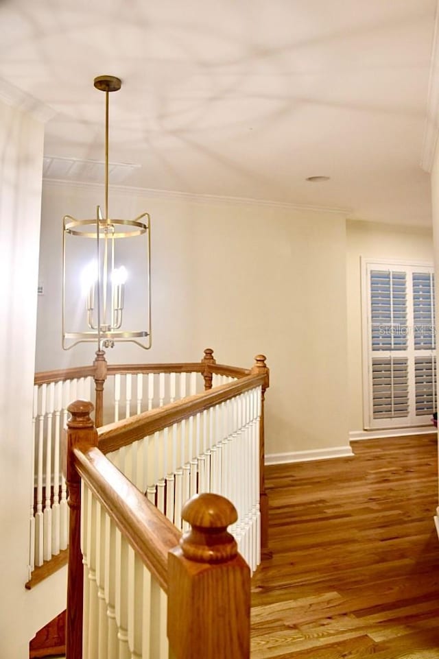 corridor with hardwood / wood-style flooring, ornamental molding, and a notable chandelier