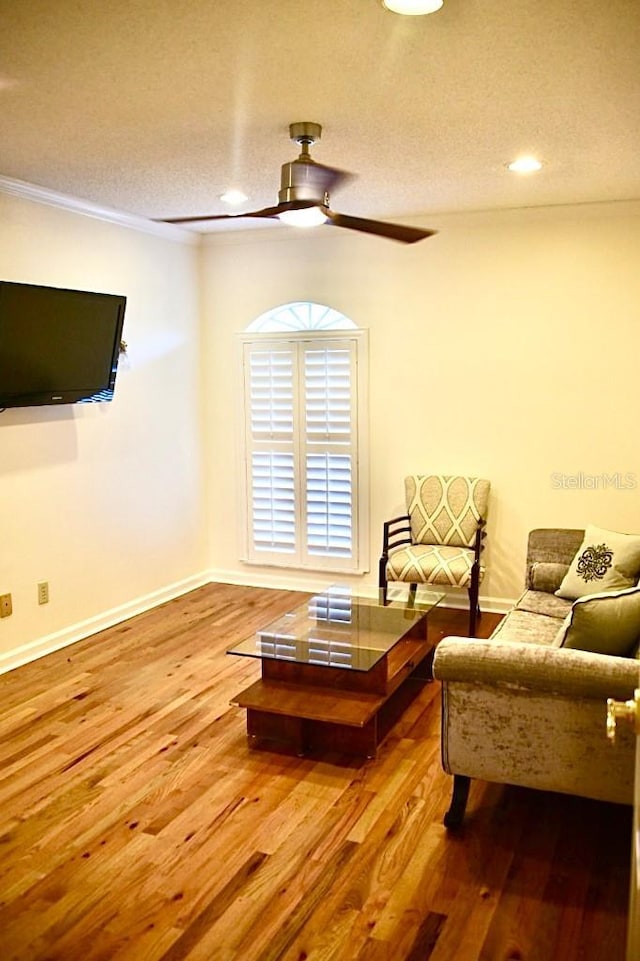 living room featuring ceiling fan, crown molding, hardwood / wood-style floors, and a textured ceiling