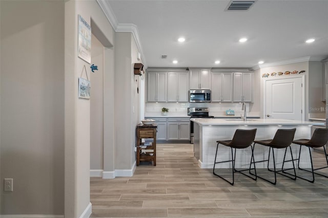 kitchen featuring tasteful backsplash, stainless steel appliances, a breakfast bar, and a center island with sink