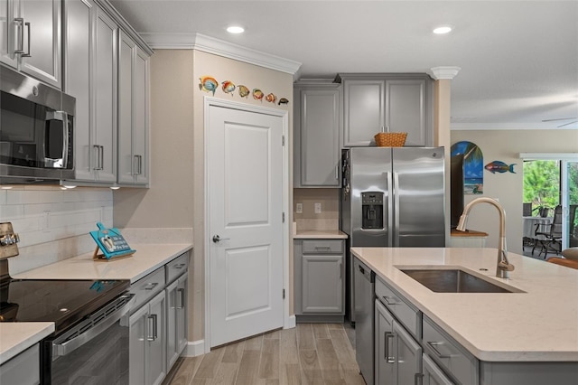 kitchen featuring gray cabinets, sink, ornamental molding, stainless steel appliances, and light wood-type flooring