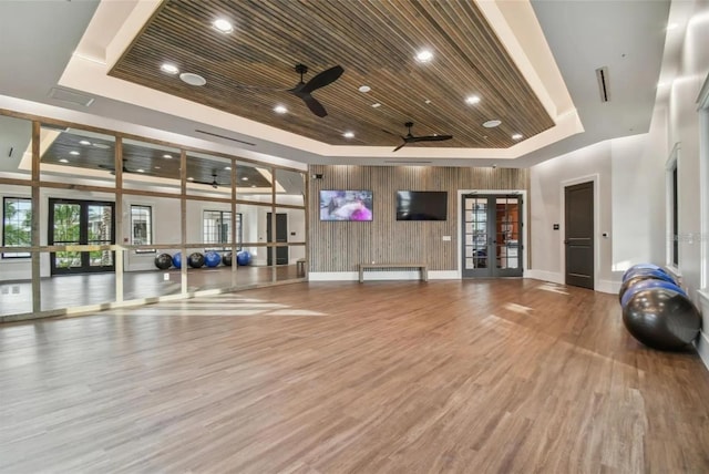 workout area featuring a tray ceiling, hardwood / wood-style flooring, ceiling fan, wood ceiling, and french doors