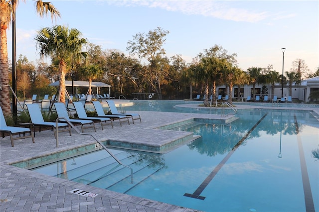 pool at dusk featuring a hot tub and a patio