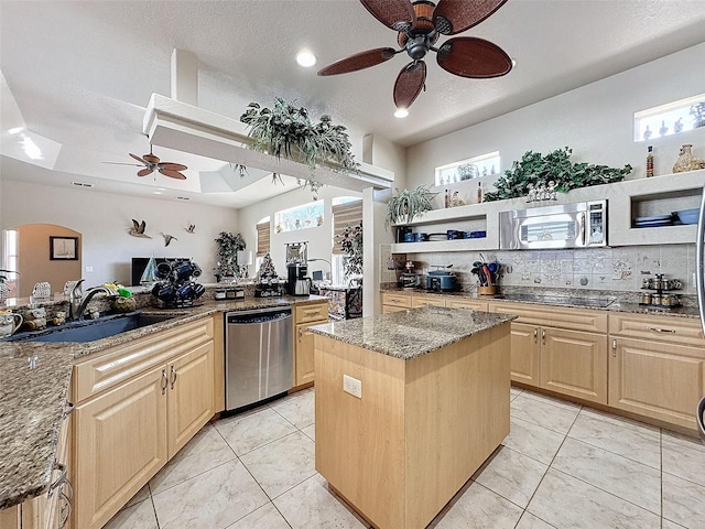 kitchen featuring stone counters, a kitchen island, a raised ceiling, sink, and stainless steel appliances