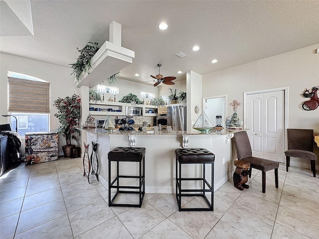 kitchen featuring a textured ceiling, kitchen peninsula, ceiling fan, and a breakfast bar