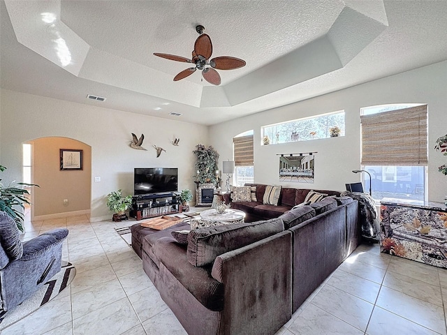 living room with ceiling fan, a textured ceiling, and a tray ceiling