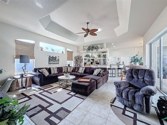 living room featuring ceiling fan, a tray ceiling, a wealth of natural light, and a textured ceiling