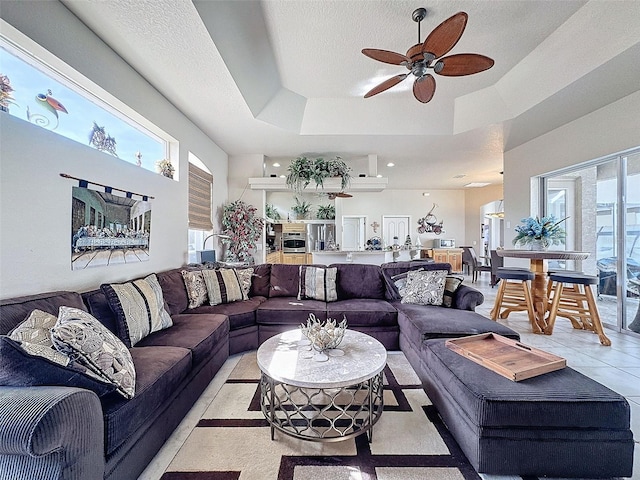 tiled living room with a healthy amount of sunlight, a textured ceiling, ceiling fan, and a tray ceiling