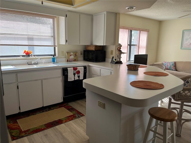 kitchen with a breakfast bar, black appliances, sink, white cabinets, and kitchen peninsula