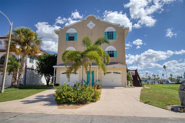 view of front of property with a front yard, concrete driveway, stairway, and stucco siding