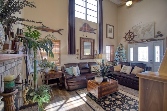 living room featuring a towering ceiling, plenty of natural light, a fireplace, and wood finished floors