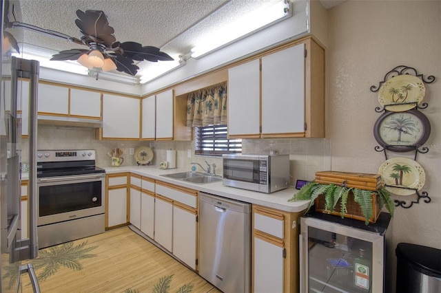 kitchen with beverage cooler, stainless steel appliances, light countertops, under cabinet range hood, and a sink