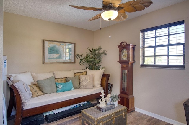 living room with ceiling fan, a textured ceiling, baseboards, and wood finished floors