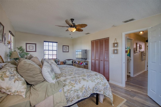 bedroom with a textured ceiling, wood finished floors, visible vents, a ceiling fan, and a closet