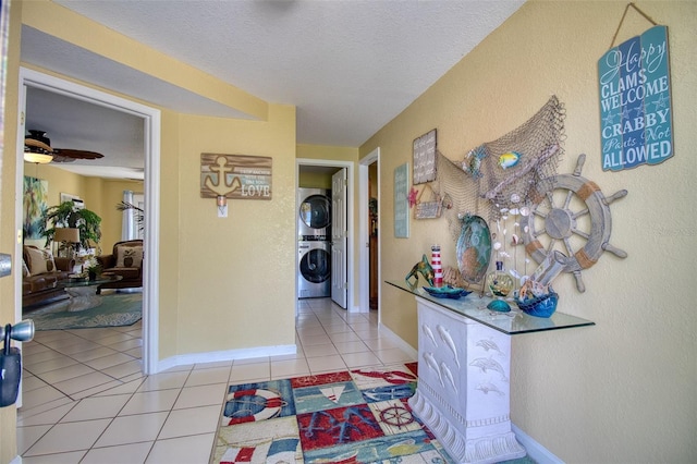 corridor with stacked washer and dryer, a textured ceiling, baseboards, and light tile patterned floors