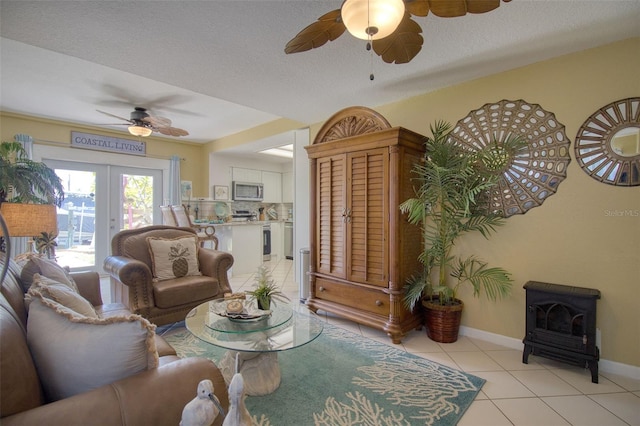 living room featuring light tile patterned floors, baseboards, a ceiling fan, a wood stove, and a textured ceiling