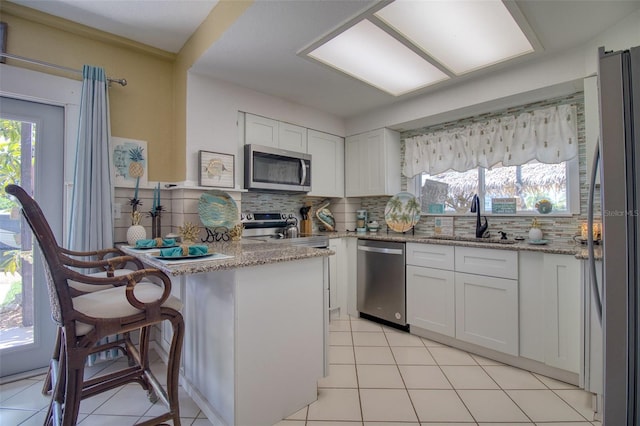 kitchen featuring sink, light stone counters, white cabinets, stainless steel appliances, and backsplash