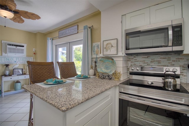 kitchen with tasteful backsplash, an AC wall unit, appliances with stainless steel finishes, light stone countertops, and white cabinets