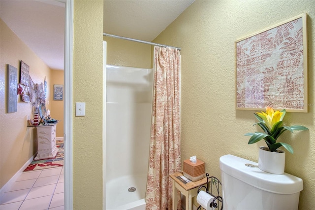 bathroom featuring baseboards, a textured wall, toilet, tile patterned flooring, and a shower stall