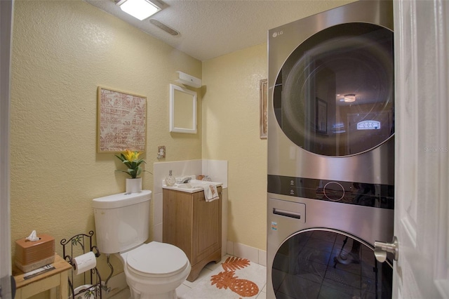 bathroom with stacked washer and dryer, a textured wall, toilet, a textured ceiling, and vanity