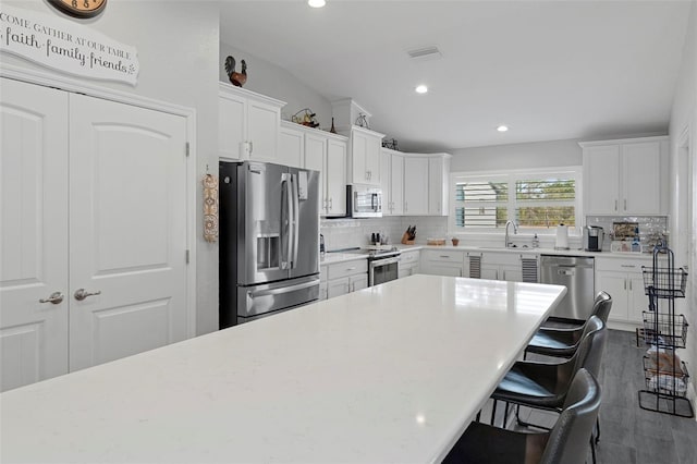 kitchen with sink, white cabinetry, stainless steel appliances, decorative backsplash, and vaulted ceiling