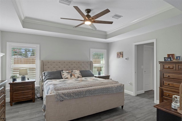 bedroom with crown molding, light wood-type flooring, and a tray ceiling