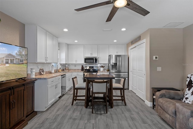 kitchen featuring white cabinetry, a kitchen breakfast bar, stainless steel appliances, light hardwood / wood-style floors, and decorative backsplash