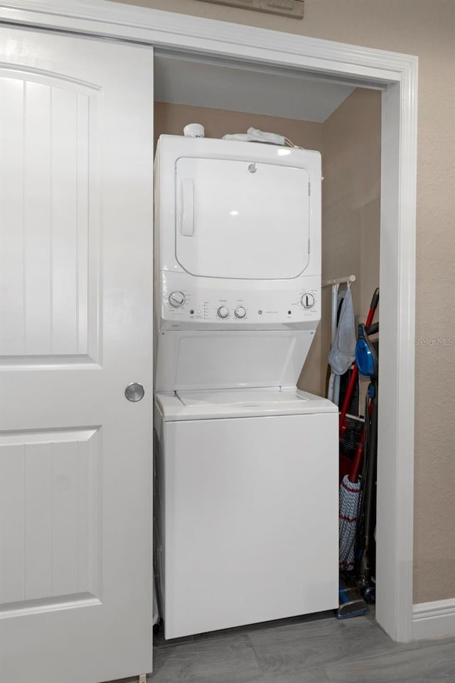 laundry area with hardwood / wood-style flooring and stacked washer and clothes dryer