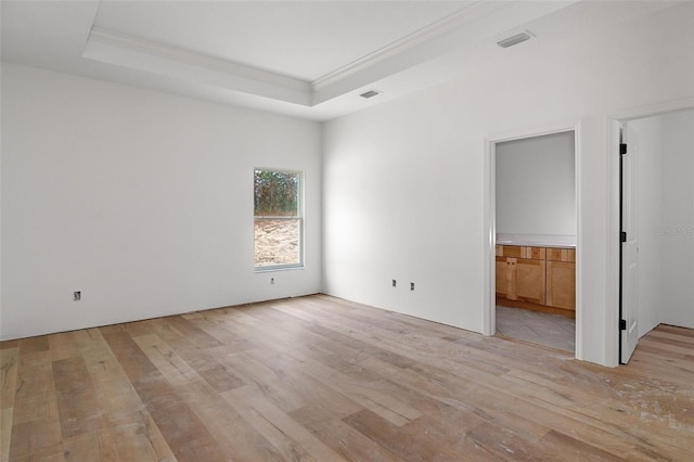 unfurnished room with a raised ceiling, crown molding, and light wood-type flooring