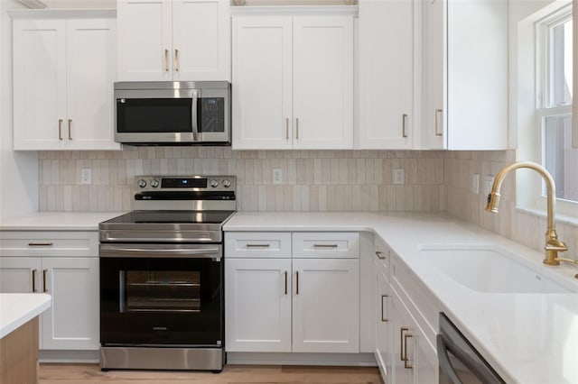 kitchen with sink, backsplash, stainless steel appliances, white cabinets, and light wood-type flooring