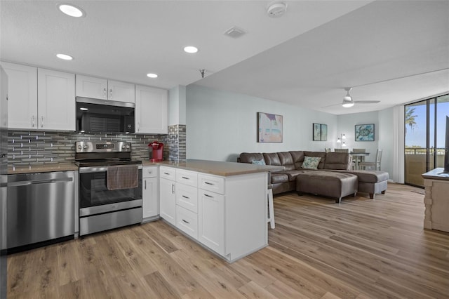 kitchen with light hardwood / wood-style flooring, kitchen peninsula, white cabinets, and appliances with stainless steel finishes